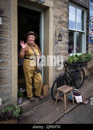 Haworth 1940 nostalgisches Retro-Ereignis mit Lebensgeschichte (Frau im Vintage WW2-Kostüm, die vor der Haustür posiert) - Main Street, West Yorkshire England. Stockfoto