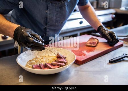 Der Chefkoch platziert Steakscheiben in einer Schüssel auf der Theke in der Restaurantküche Stockfoto