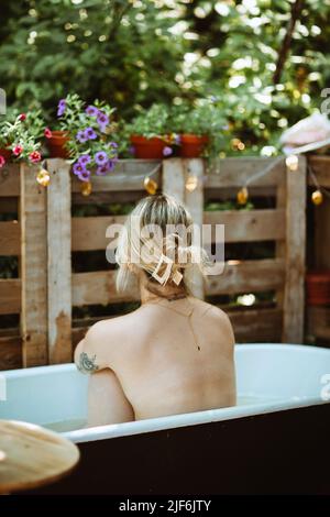 Seitenansicht einer anmutigen Frau im Sommerkleid, die am Tisch auf dem Balkon sitzt und wegschaut Stockfoto