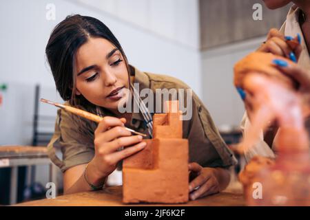 Young Hispanic female artisan with dark hair carving geometric shape from clay on table in light studio in daytime Stockfoto