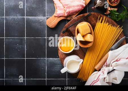 Zutaten für Pasta Carbonara. Traditionelle italienische Pasta Carbonara Zutaten Speck, Spaghetti, Parmesan und Eigelb, Knoblauch. Schwarzer alter Kacheltisch Stockfoto