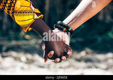 Liebevolle multiethnische Menschen mit Holzperlenarmband, das die Hände hält und sich verbindet, während Sie an sonnigen Sommertagen in der Natur zusammen spazieren Stockfoto