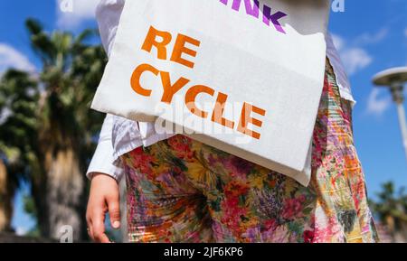 Crop anonyme weibliche Tragetasche mit Re Think Re Cycle Inschrift, während in der Nähe von Zaun auf der Straße am Sommertag stehen Stockfoto