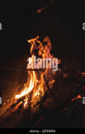 Von oben brennendes Feuerholz mit hellen orangen Flammen auf dem Boden des Campingplatzes in der dunklen Nacht Stockfoto