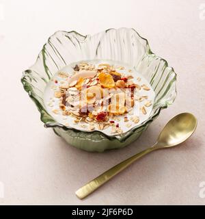 Schüssel mit Joghurt und Frühstückscerealien neben einem Metalllöffel auf einem Tisch Stockfoto