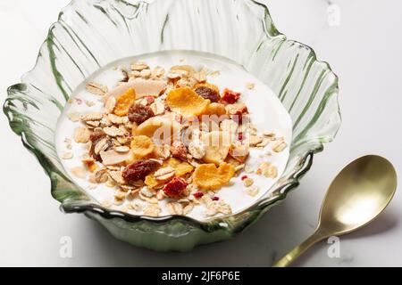 Schüssel mit Joghurt und Frühstückscerealien neben einem Metalllöffel auf einem Tisch Stockfoto