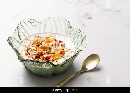 Schüssel mit Joghurt und Frühstückscerealien neben einem Metalllöffel auf einem Tisch Stockfoto