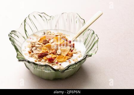 Schüssel mit Joghurt und Frühstückszerealien mit einem Metalllöffel auf einem Tisch Stockfoto