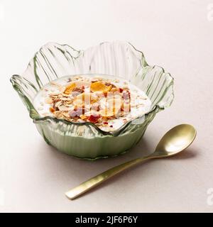 Schüssel mit Joghurt und Frühstückscerealien neben einem Metalllöffel auf einem Tisch Stockfoto