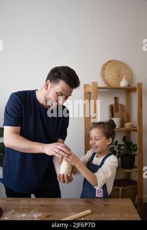 Lächelnder Vater und Tochter halten den Teig zu Hause neben dem Tisch Stockfoto