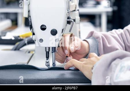 Crop anonyme Schneiderin mit Nahtripper auf Textil in der Nähe von speziellen Nähmaschine während der Arbeit in professionellen Licht-atelier Stockfoto