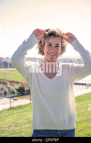 Porträt einer lächelnden reifen Frau mit Sonnenbrille, die im Sommer auf der Wiese steht Stockfoto
