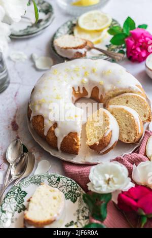 Oben Biskuit Zitronenkuchen auf einem Tisch neben anderen Tellern mit Zitronenscheiben und Blumen mit Blütenblättern Stockfoto