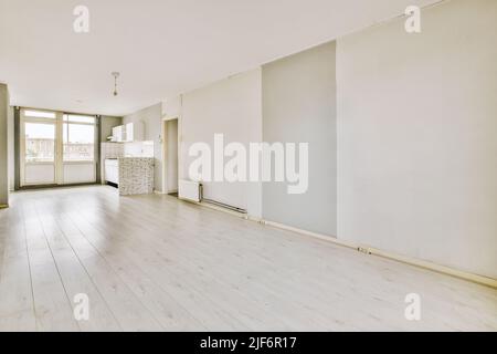 Die Einrichtung einer leeren, offenen, weißen Küche mit Fenstern und Holzparkettboden Stockfoto