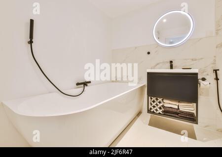 Badewanne mit Glasdusche in der Ecke neben Waschbecken und Spiegel im kleinen hellen Badezimmer mit weißen Kachelwänden Stockfoto