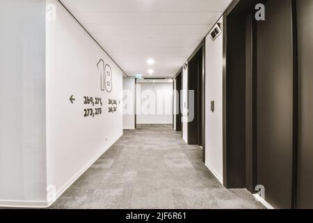 Glänzender Aufzug mit geöffneter Tür in der beleuchteten Halle eines modernen Apartmentgebäudes mit Fliesenboden Stockfoto