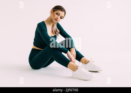 Im Fitnessstudio sitzt eine junge Fitnessfrau auf dem Boden. Stockfoto