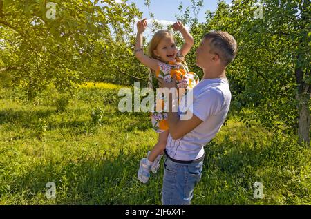 Glückliches kleines Mädchen in den Armen ihres Vaters. Tochter spielt und lacht in der Natur. Vatertag, Vater hält fröhlich lächelnde Tochter in seinen Armen unter den Stockfoto