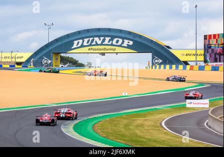 Rennwagen fahren mit der Dunlop-Schikane, bevor sie während der 24 Stunden von Le Mans unter der Dunlop-Fußgängerbrücke auf der Rennstrecke Circuit de la Sarthe fahren. Stockfoto