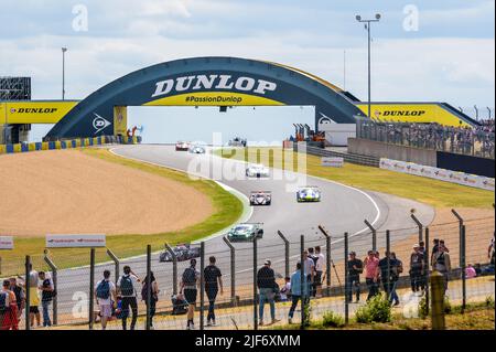 Rennwagen fahren unter der Dunlop-Fußgängerbrücke hindurch und fahren während der 24 Stunden von Le Mans die Kurven auf der Rennstrecke Circuit de la Sarthe hinunter. Stockfoto