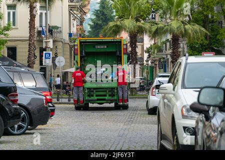 Batumi, Georgia - Mai 31 2022: Zwei Plünderer arbeiten zusammen, um Mülltonnen für die Müllentsorgung zu leeren, indem sie einen LKW zum Verladen von Abfällen benutzen. Konzept der Ökologie Stockfoto