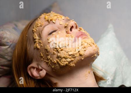 Eine Frau macht zu Hause eine kosmetische Maske aus Haferflocken auf ihr Gesicht. Anti-Aging-Behandlungen, Hautpflegekonzept. Stockfoto