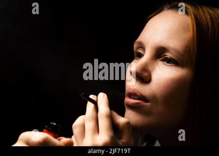 Frau raucht Marihuana, Cannabis durch ein Gerät auf schwarzem Hintergrund. Stockfoto