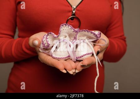 Eine Schwangerin hält weiße gestrickte Stiefelchen in den Händen Stockfoto