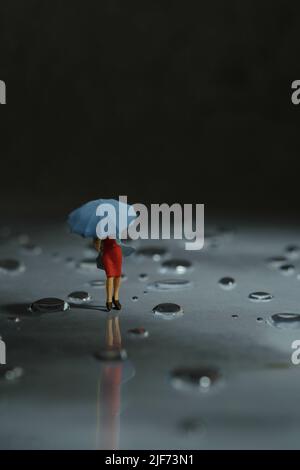 Miniatur Menschen Spielzeug Figur Fotografie. Eine Frau, die einen Regenmantel mit Regenschirm trägt und während eines Sturms auf der Straße läuft, gegen einen sehr starken Wind. Stockfoto