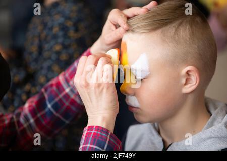 Make-up-Künstler zeichnet Gesichtsbemalung auf das Gesicht eines kleinen Jungen. Stockfoto