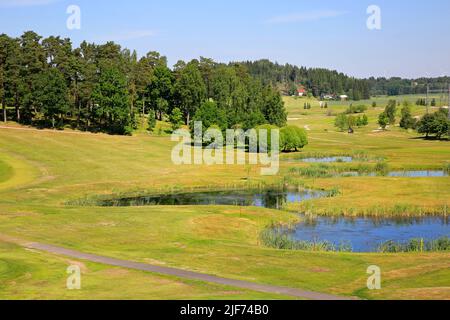Blick auf einen idyllischen Golfplatz an einem schönen Sommertag mit kleinen Teichen und Wald. Stockfoto