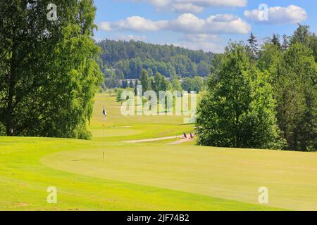 Blick auf einen idyllischen Golfplatz an einem schönen Sommertag mit Golfflagge, Bäumen und blauem Himmel mit Wolken. Stockfoto