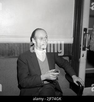 1961, historisch, sitzend auf einem Stuhl in einem Krankenhauskorridor, der Lord Montagu von Beaulieu mit einem Glas Champagner in der Hand, feiert die Geburt seines ersten Sohnes, Ralph Douglas-Scott-Montagu, 4. Baron Montagu von Beaulieu. Der Familiensitz, das Beaulieu Estate in Hampshire, England, mit dem Beaulieu Palace House, einem Gebäude aus dem 13.. Jahrhundert, das ursprünglich Teil der Beaulieu Abbey war, beherbergt das 1952 gegründete National Motor Museum. Montagu, eine Figur von nationaler Bedeutung, hielt sein Peerage für die drittlängste in der Geschichte Briitschs, insgesamt 86 Jahre und 155 Tage. Stockfoto