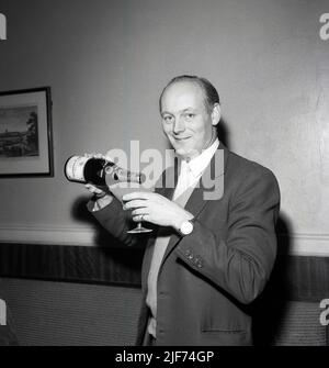 1961, historisch, der Lord Montagu von Beaulieu mit einem Glas und einer Flasche Champagner in der Hand, feiert die Geburt seines ersten Sohnes, Ralph Douglas-Scott-Montagu, 4. Baron Montagu von Beaulieu. Der Familiensitz, das Beaulieu Estate in Hampshire, England, mit dem Beaulieu Palace House, einem Gebäude aus dem 13.. Jahrhundert, das ursprünglich zur Beaulieu Abbey gehört, beherbergt das 1952 gegründete National Motor Museum. Montagu, eine Figur von nationaler Bedeutung, hielt sein Peerage für die drittlängste in der Geschichte Briitschs, insgesamt 86 Jahre und 155 Tage. Stockfoto