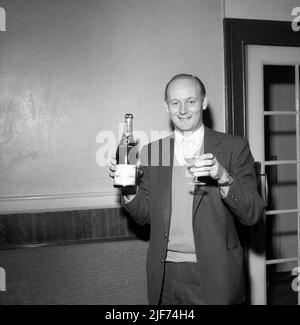 1961, historisch, der Lord Montagu von Beaulieu mit einer Flasche und einem Glas Champagner in der Hand, feiert die Geburt seines ersten Sohnes, Ralph Douglas-Scott-Montagu, 4. Baron Montagu von Beaulieu. Der Familiensitz, das Beaulieu Estate in Hampshire, England, mit dem Beaulieu Palace House, einem Gebäude aus dem 13.. Jahrhundert, das ursprünglich Teil der Beaulieu Abbey war, beherbergt das 1952 gegründete National Motor Museum. Montagu, eine Figur von nationaler Bedeutung, hielt sein Peerage für die drittlängste in der Geschichte Briitschs, insgesamt 86 Jahre und 155 Tage. Stockfoto