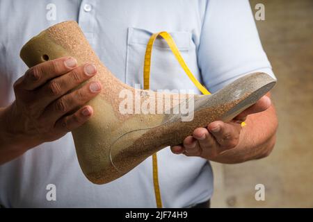 Nahaufnahme der Hände eines orthopädischen Schuhmachers, der eine individuell gefertigte Holzschnur präsentiert Stockfoto