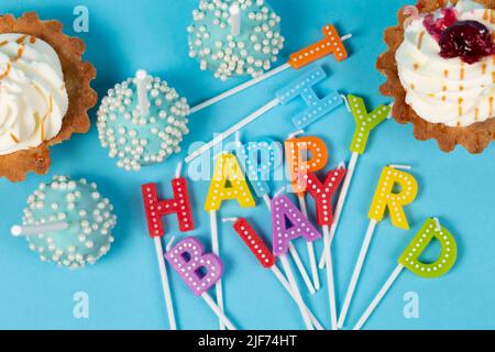 Kuchen und Cupcakes mit regenbogenfarbenen Geburtstagskerzen mit den Worten Alles Gute zum Geburtstag. Jubiläumsfeier. Stockfoto