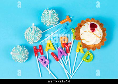 Kuchen und Cupcakes mit regenbogenfarbenen Geburtstagskerzen mit den Worten Alles Gute zum Geburtstag. Jubiläumsfeier. Stockfoto