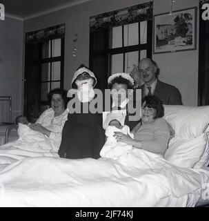 1965, historisch, ein Weihnachtsvater, der eine Entbindungsstation besucht und für ein Foto steht, beisde eine Krankenschwester und zwei neue Mütter, die mit ihren neuen Babys in Krankenhausbetten liegen, Fife, Schottland, Großbritannien. Stockfoto