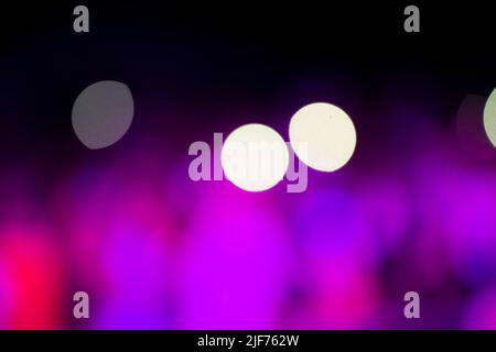 Auf schwarzem Hintergrund große weiße und violette Bokeh-Flecken. Stockfoto
