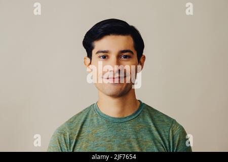 Headshot Latino Mann schwarzes Haar lächelnd schönes junges Erwachsener grünes T-Shirt über grauem Hintergrund Blick auf Kamera Studio aufgenommen Stockfoto