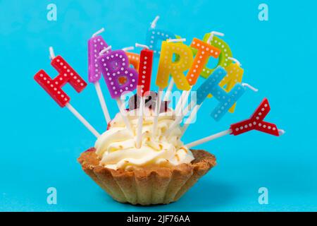 Cupcake mit regenbogenfarbenen Kerzen zum Geburtstag mit der Aufschrift 'Happy Birthday' Stockfoto