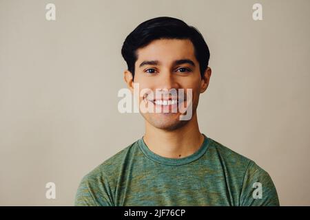 Headshot Latino Mann schwarzes Haar lächelnd schönes junges Erwachsener grünes T-Shirt über grauem Hintergrund Blick auf Kamera Studio aufgenommen Stockfoto