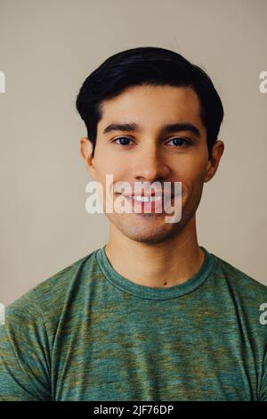 Headshot Latino Mann schwarzes Haar lächelnd schönes junges Erwachsener grünes T-Shirt über grauem Hintergrund Blick auf Kamera Studio aufgenommen Stockfoto