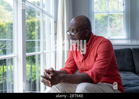 Nachdenklicher reifer afroamerikanischer Mann, der durch das Fenster schaute, während er zu Hause saß, Platz kopieren Stockfoto