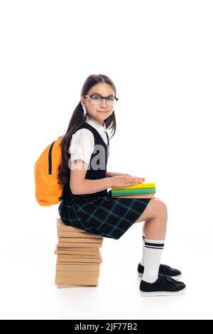 Lächelndes Schulkind mit Rucksack auf Büchern auf weißem Hintergrund Stockfoto