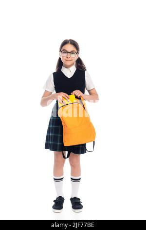 Volle Länge der fröhlichen Schüler Putting Buch im Rucksack auf weißem Hintergrund Stockfoto