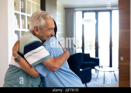 Kaukasischer älterer Mann und biraziale weibliche Gesundheitshelferin umarmen sich zu Hause Stockfoto