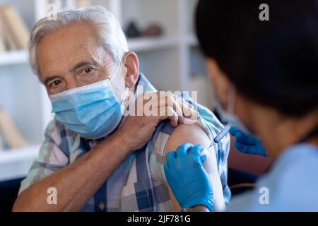 Biraziale Gesundheitshelferin, die zu Hause dem älteren kaukasischen Mann eine Injektion verabreicht Stockfoto