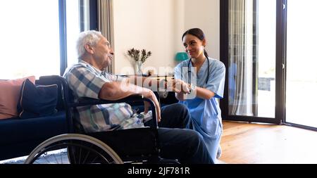 Biraziale Gesundheitshelferin, die einen kaukasischen älteren Mann unterstützt, der auf dem Rollstuhl sitzt Stockfoto